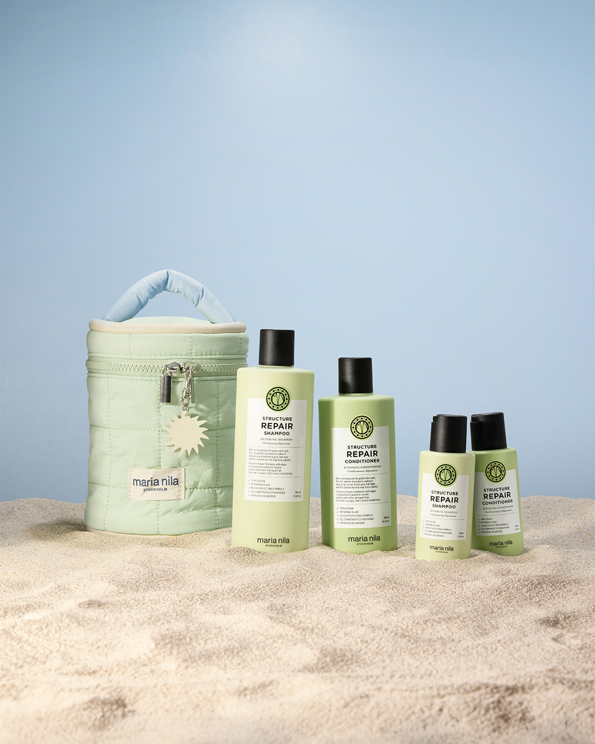 Set of hair care products and a Beauty Bag on sand with a light blue background.