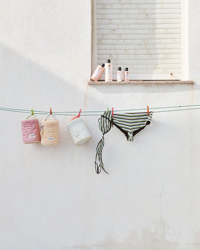 Bathing suits and Beauty Bags hanging on a clothesline against a white wall.