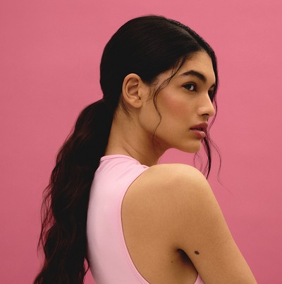 Model with dark hair in a low ponytail against pink background