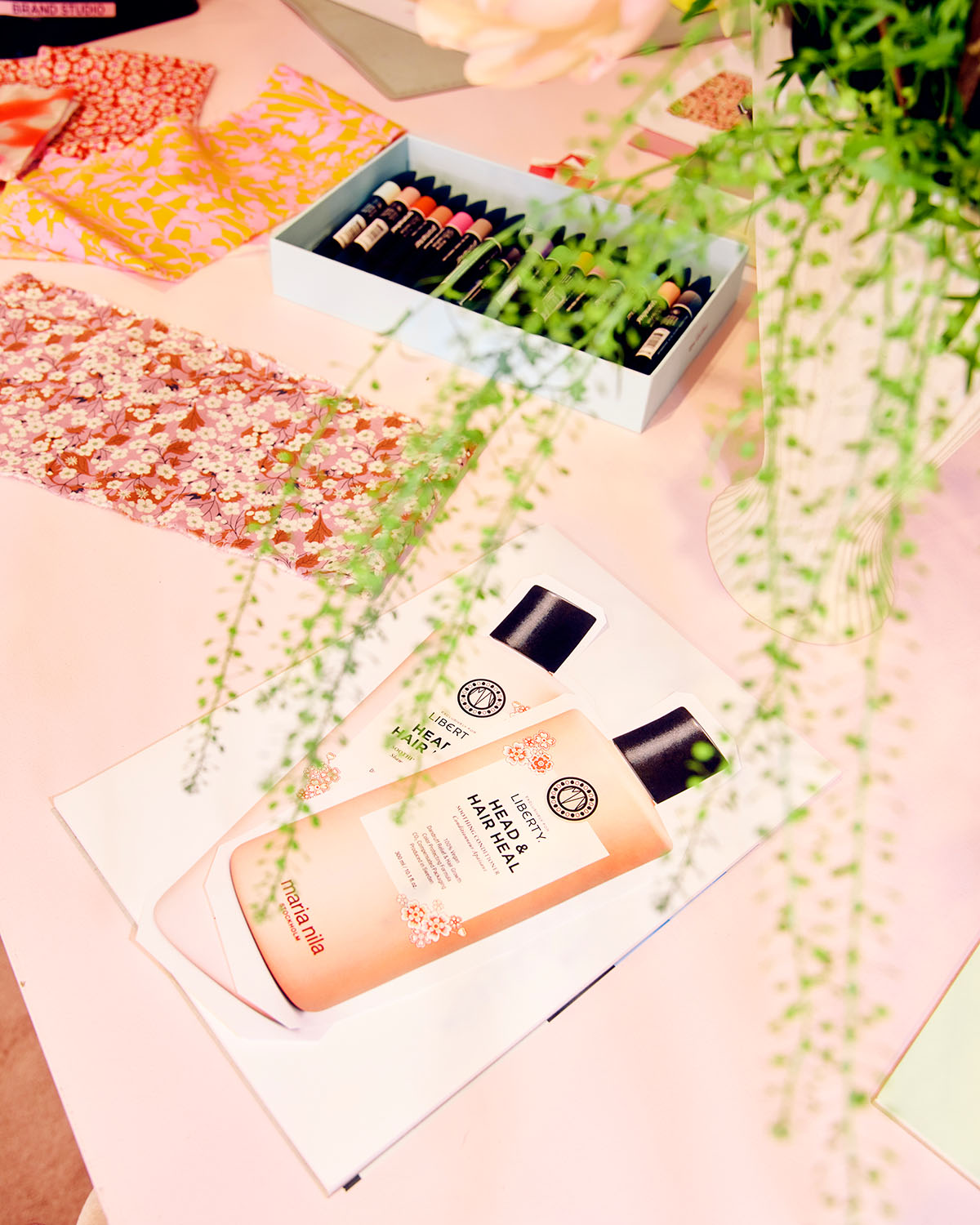 Shampoo and Conditioner with floral design packaging on a pink surface with green leaves.